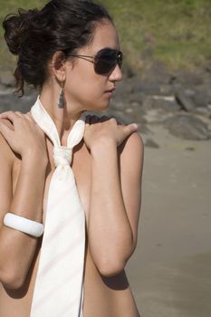 A young brazilian brunette wearing a white tie and aviator sunglasses on the beach.