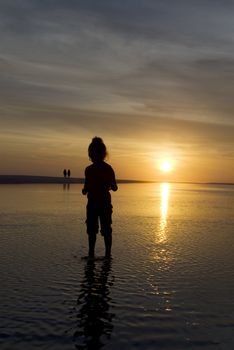 A young girl staring curiously at the ripples in a wading pool as the sun sets beautifully in the background