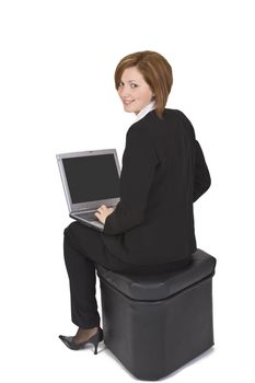 Businesswoman sitting on a pouffe with a laptop in her lap and looking up back over the shoulder.
