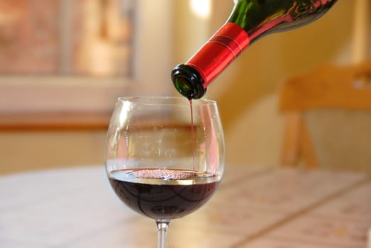 pouring red wine into wineglass from green bottle