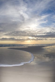 The setting sun reflects off the water as the surf flows in and the clouds glow on the horizon