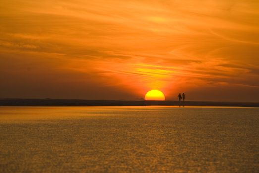 A couple walks along the beach during sunset with a spectacularly colorful sky