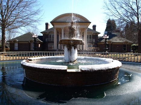 A cold frozen fountain and pond in front of a mansio