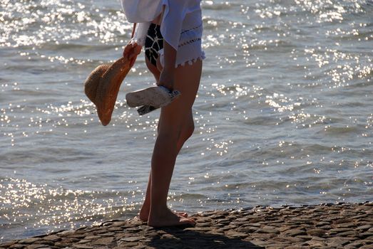 woman in swim suit with hat standing by shining seawater