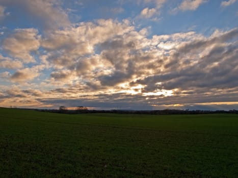 Dramatic sunset with cloudscape over a green field background