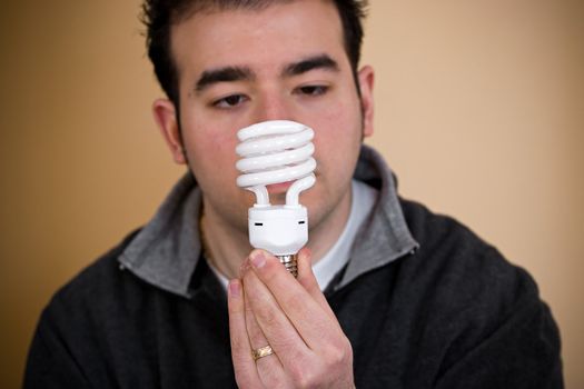 A young man holding an energy saving compact fluorescent light bulb.  Shallow depth of field with stronger focus on the bulb.