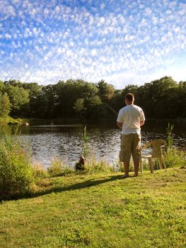 A lone fishermen fishing in a rural pond.