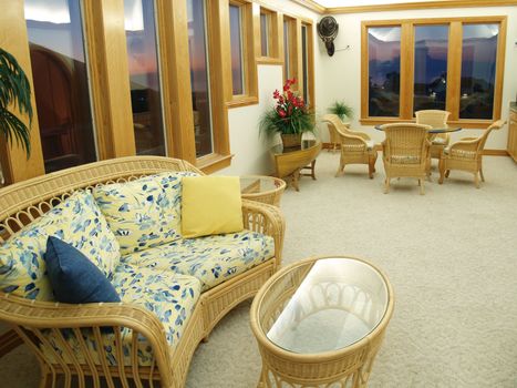 Comfortable lounge room in an expensive beach vacation home. Wicker and rattan furniture and a glass topped table decorate the interior.