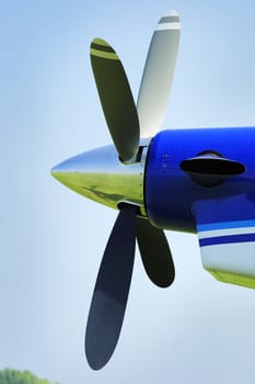 The propeller of an aircraft against a clear blue sky. The grass airstrip and sky can be seen reflected in the nose cone.