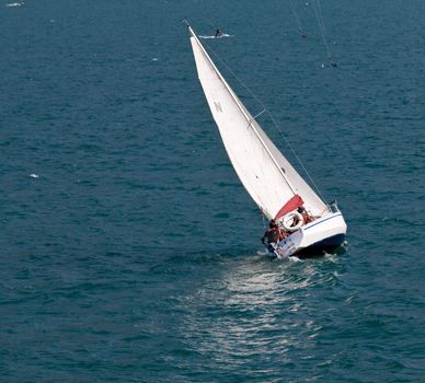 Yacht on Lake Garda sailing between parasurfing athletes