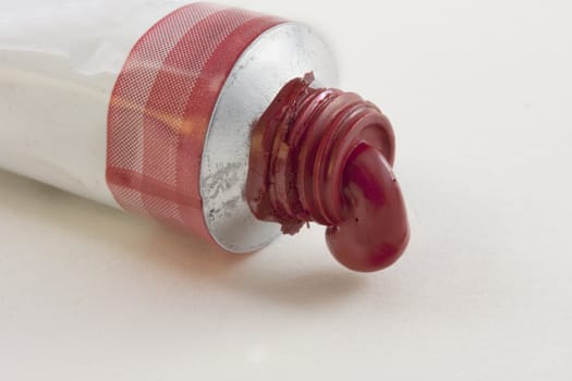 open tube of watercolor red paint against white textured paper background
