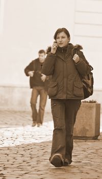 Redheaded girl student at the phone while is walking on a paved street-sepia tones.