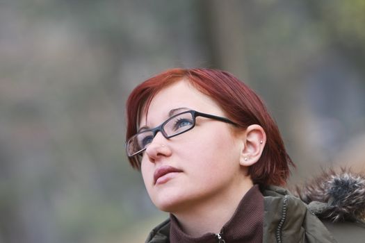 Portrait of a redheaded girl with glasses against a blurred autumn background. 