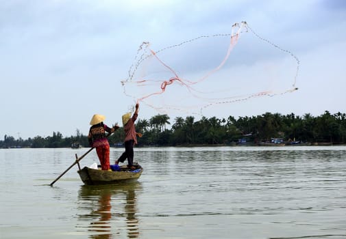 A view of two fishermen in action with their net in a little boat on the Mekong river