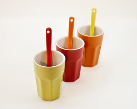 Three colored ceramic glasses with spoons on a white background