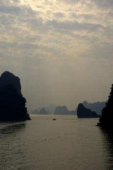 Beginning of sunset in Halong bay with some big rocks and a little boat