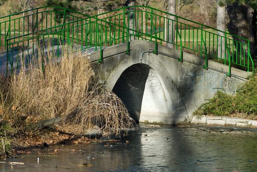 a bridge in a park which leads over a frozen creek the sun is shining bright