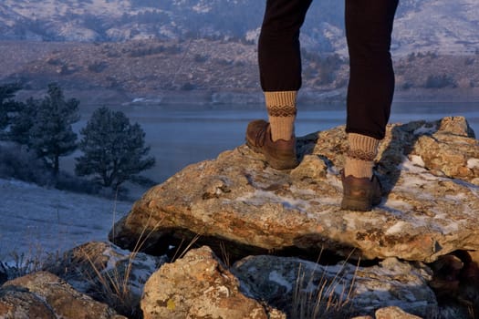 hiker or trail runner legs and feet on rock overlooking mountain lake,  winter scenery with snow, fog, frost at sunrise light in Colorado