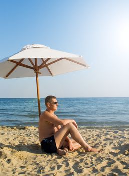 The man under a solar umbrella on a beach