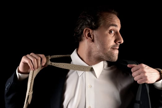 Adult businessman stressed pulling off tie on dark background