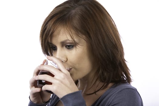 A beautiful young woman with red hair drinking a red fizzy drink from a glass