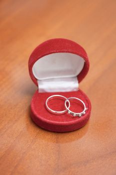 Small red casket with two wedding rings on wooden surface