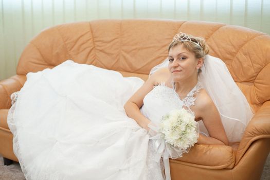 The bride comfortably lies on the big leather sofa