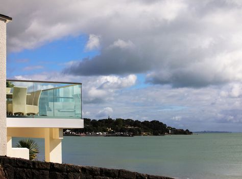 Glass balcony with furniture on a background of coast of Pacific ocean. New Zealand
