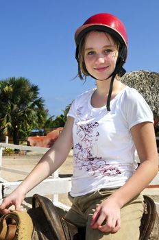 Young girl in a saddle wearing red helmet