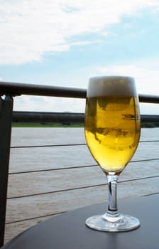 Glass of beer with river on the background.
