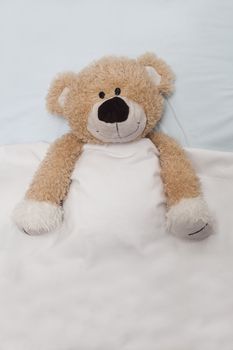 An adorable teddy bear laying in bed, under the sheets.