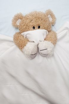 An adorable teddy bear laying in bed, scared, under the sheets.