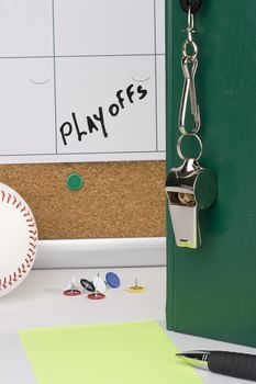 A silver whislte on a green notebook placed next to a baseball and a calendar with the playoffs date on it.