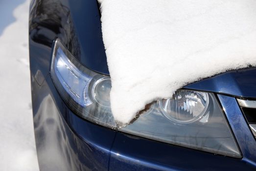 Snow covering a headlight of blue car