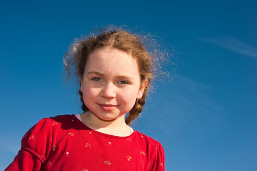 young girl looking down into camera, blue sky behind