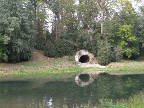 Pictoresque English garden with trees, pond, ruins of a grotto
