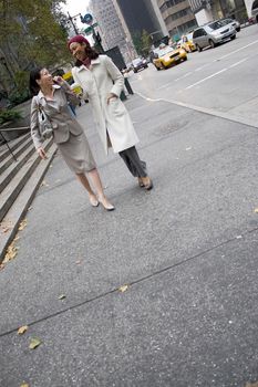 Two business women walking in the big city with plenty of copy space. One woman is on her cell phone.