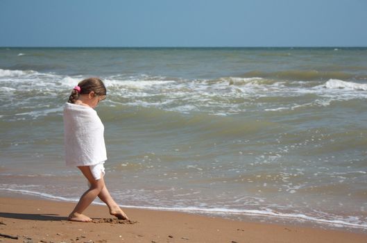  Little girl wrapped in a towel standing on the sand on the seashore
