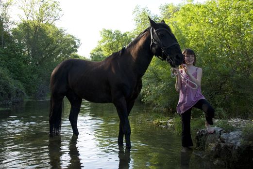 young teenager and her black horse in a river