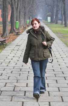 Redheaded girl walking alone in an autumn park.