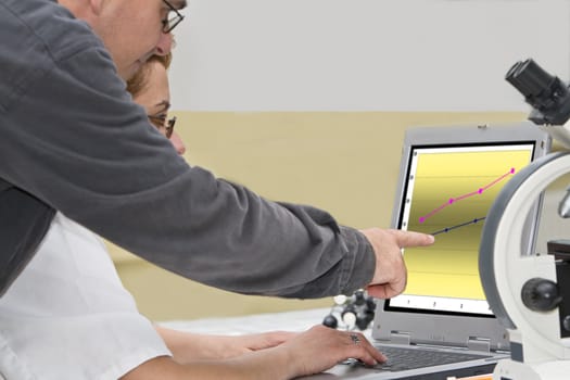 Two researcher colleagues analyzing the graph of the experiment results on a laptop-close-up.