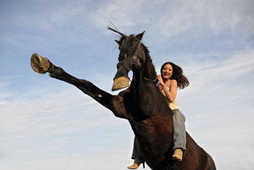 rearing black stallion and laughing girl in a blue sky. focus on the woman.