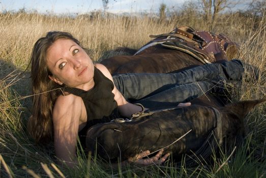 young woman and her blackhorse laid down in a field