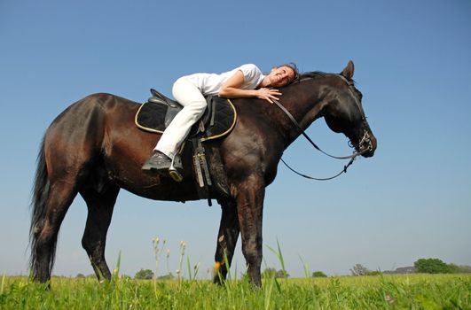 young woman and her black stallion in a field in spring
