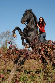 rearing black stallion and happy young girl in autumn