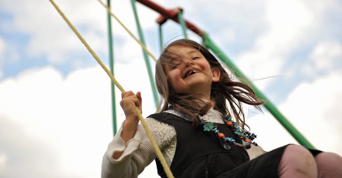 happy young girl on her swing on a cloudy sky