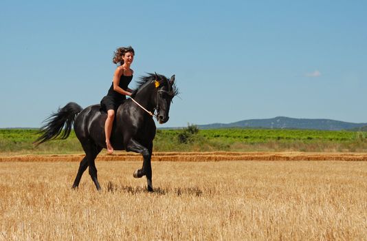 young woman and her black stallion in a field in summer