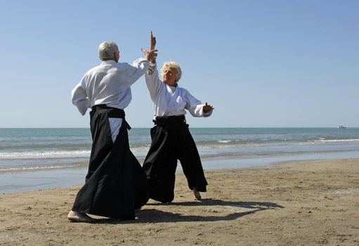 Two adults are training in Aikido on the beach