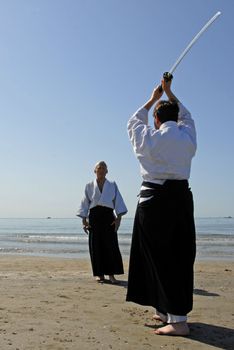 Two adults are training in Aikido on the beach