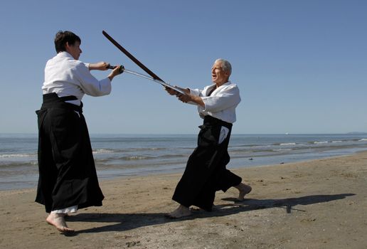 Two adults are training in Aikido on the beach